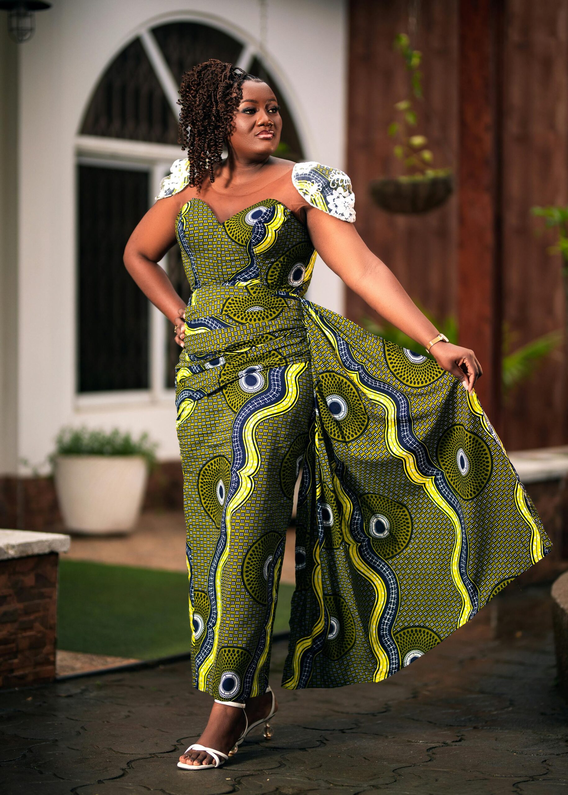 A fashionable woman posing gracefully in an African print dress outdoors, showcasing elegance and style.